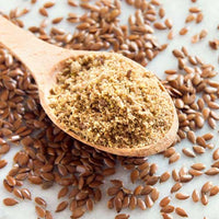 Wooden spoon filled with ground flaxseeds surrounded by whole flaxseeds on a light background