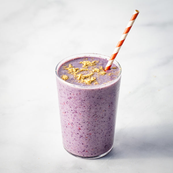 Purple smoothie in a glass with true cold milled flax on a light gray background
