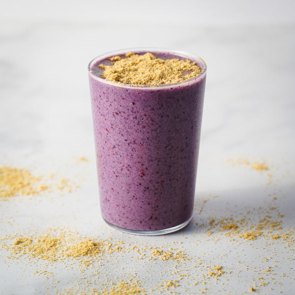 Purple smoothie in a glass with true cold milled flax on a light gray background