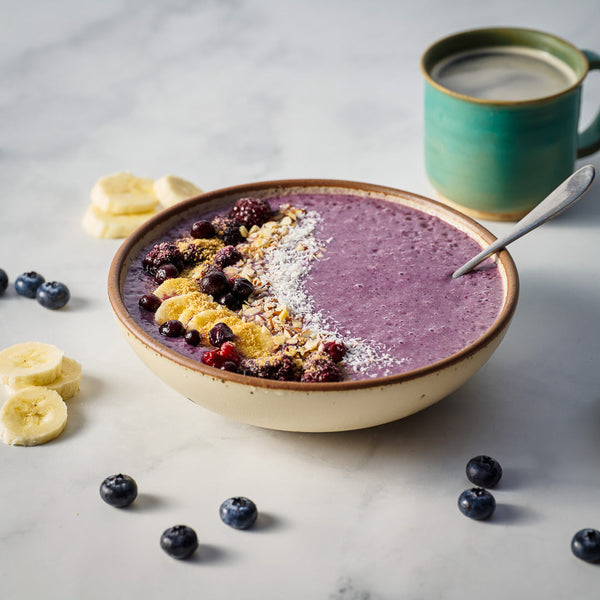 Smoothie bowl with fruit and a mug on a light surface