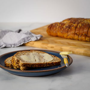 Sliced bread with butter on a blue plate on a marble surface, with a loaf of bread in the background.