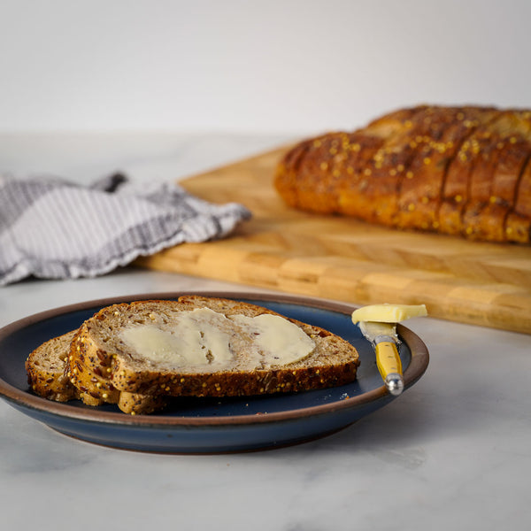Sliced bread with butter on a blue plate on a marble surface, with a loaf of bread in the background.