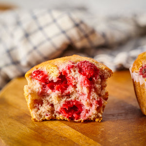 Half of a raspberry muffin on a wooden surface with a checkered cloth in the background