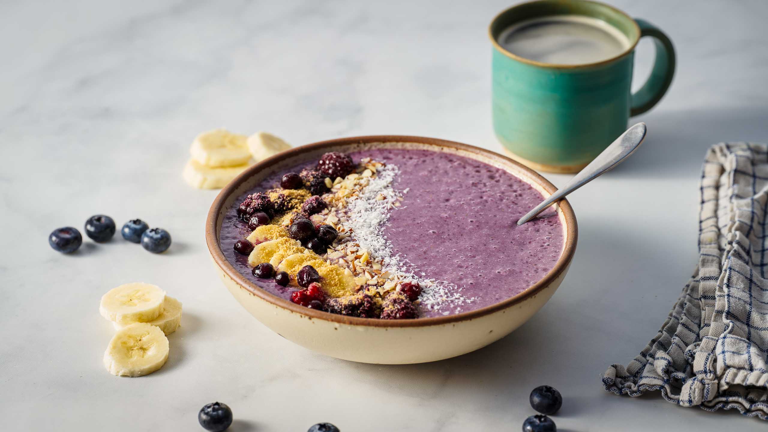 A purple smoothie bowl fruits and true cold milled ground flax on top, with a side of coffee on a light surface