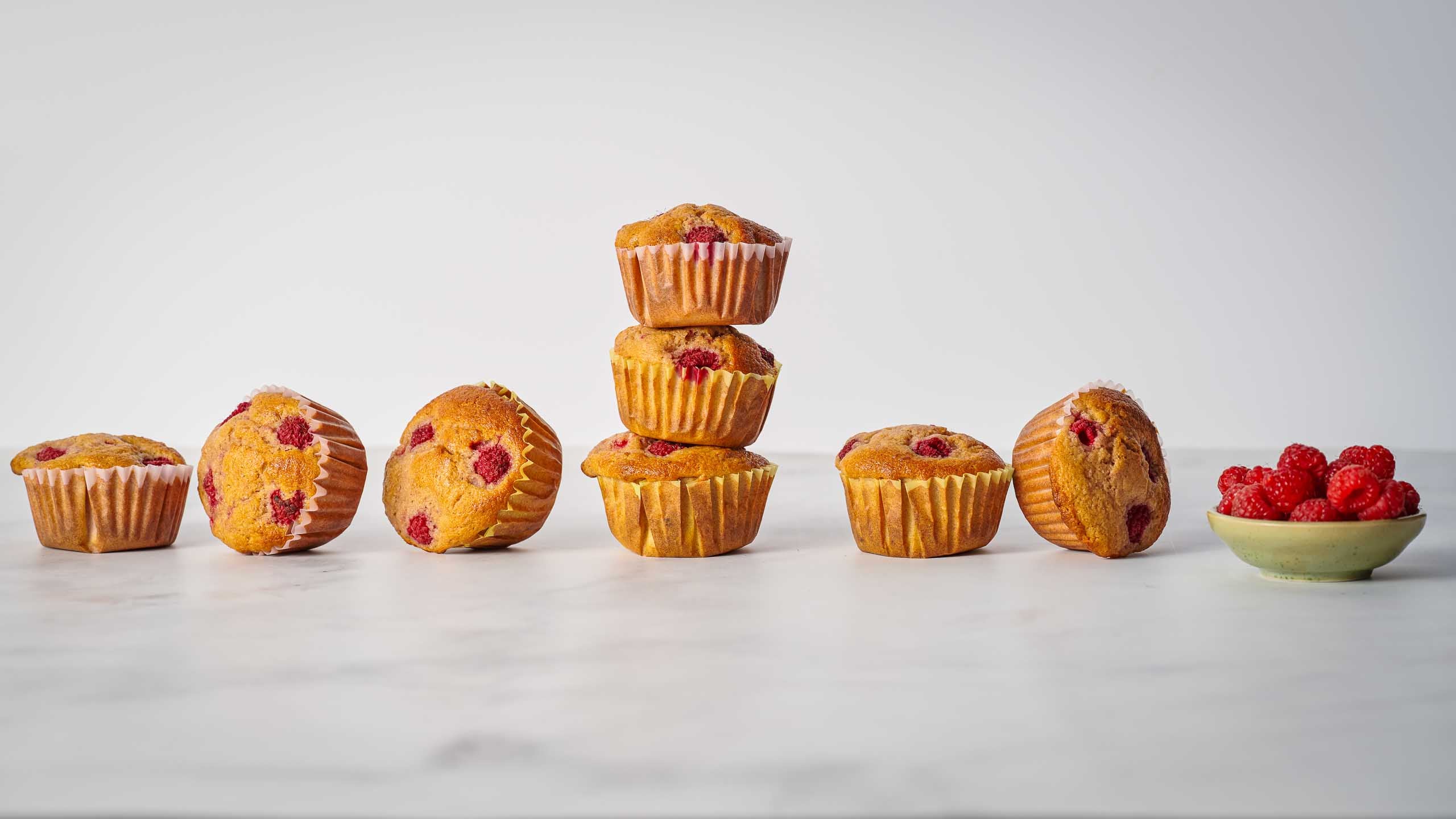 a row of raspberry muffins next to a bowl of raspberries