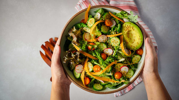 Person holding a bowl of fresh salad with whole flax seeds sprinkled on top, with hands visible