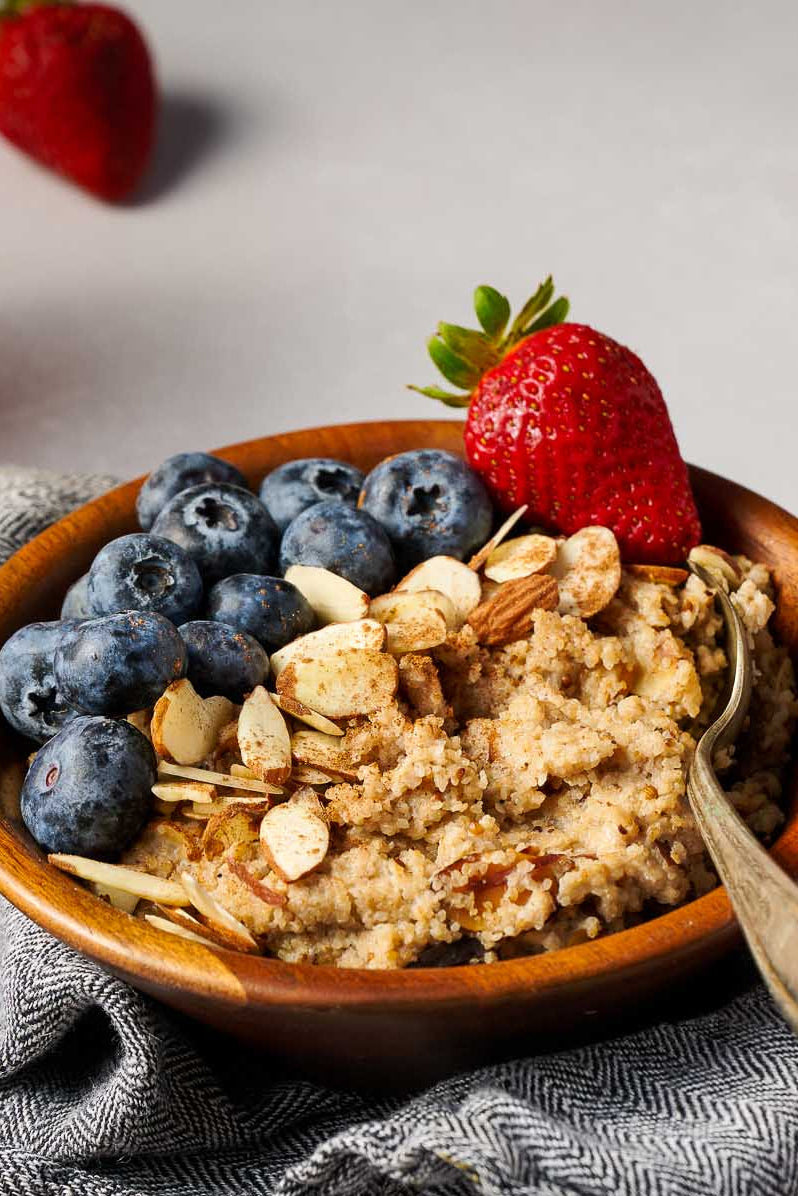 Breakfast setting with a bowl of fonio, berries, and sliced almonds on a grey surface
