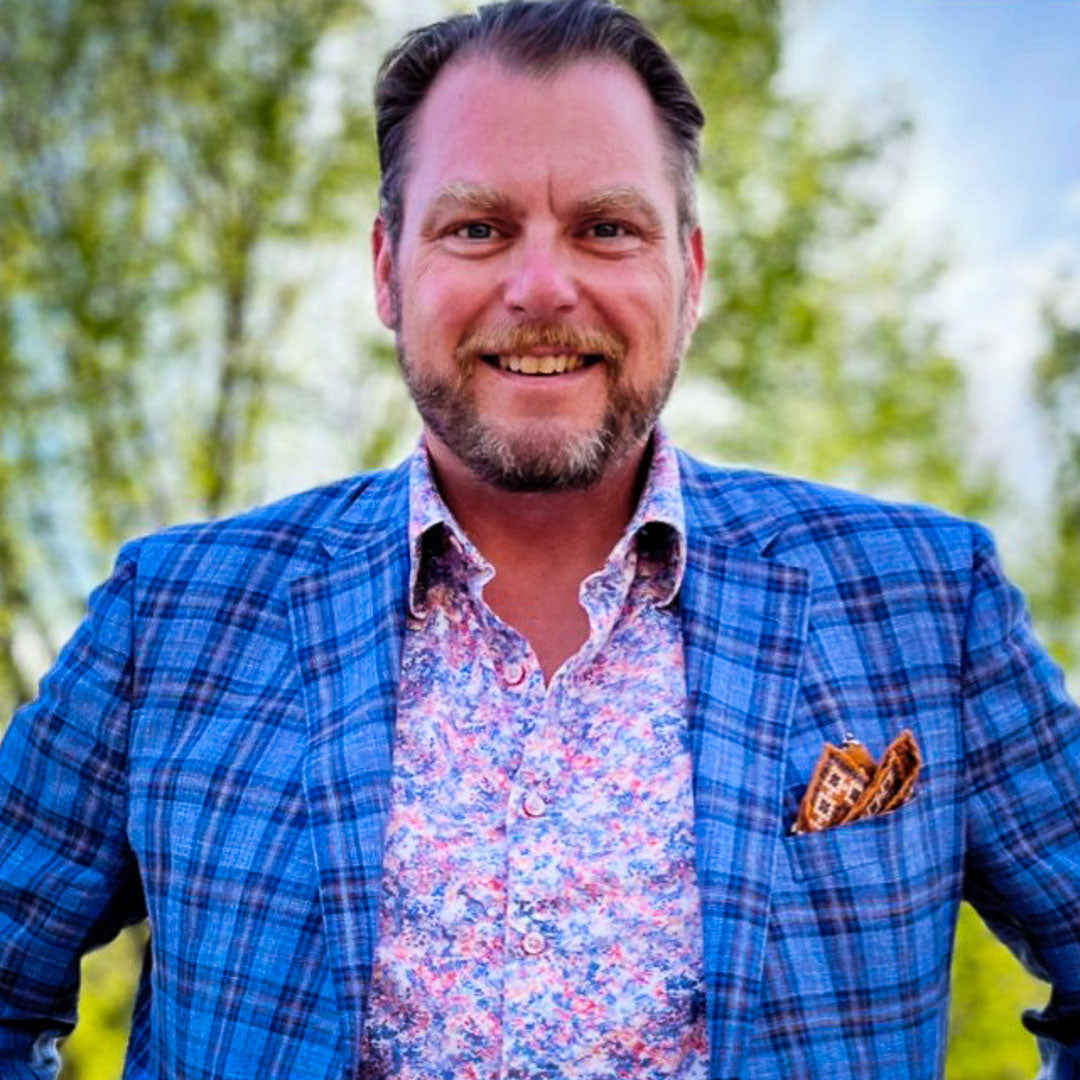 Man wearing a blue plaid jacket over a patterned shirt with a blurred green background (Mike Marshall)